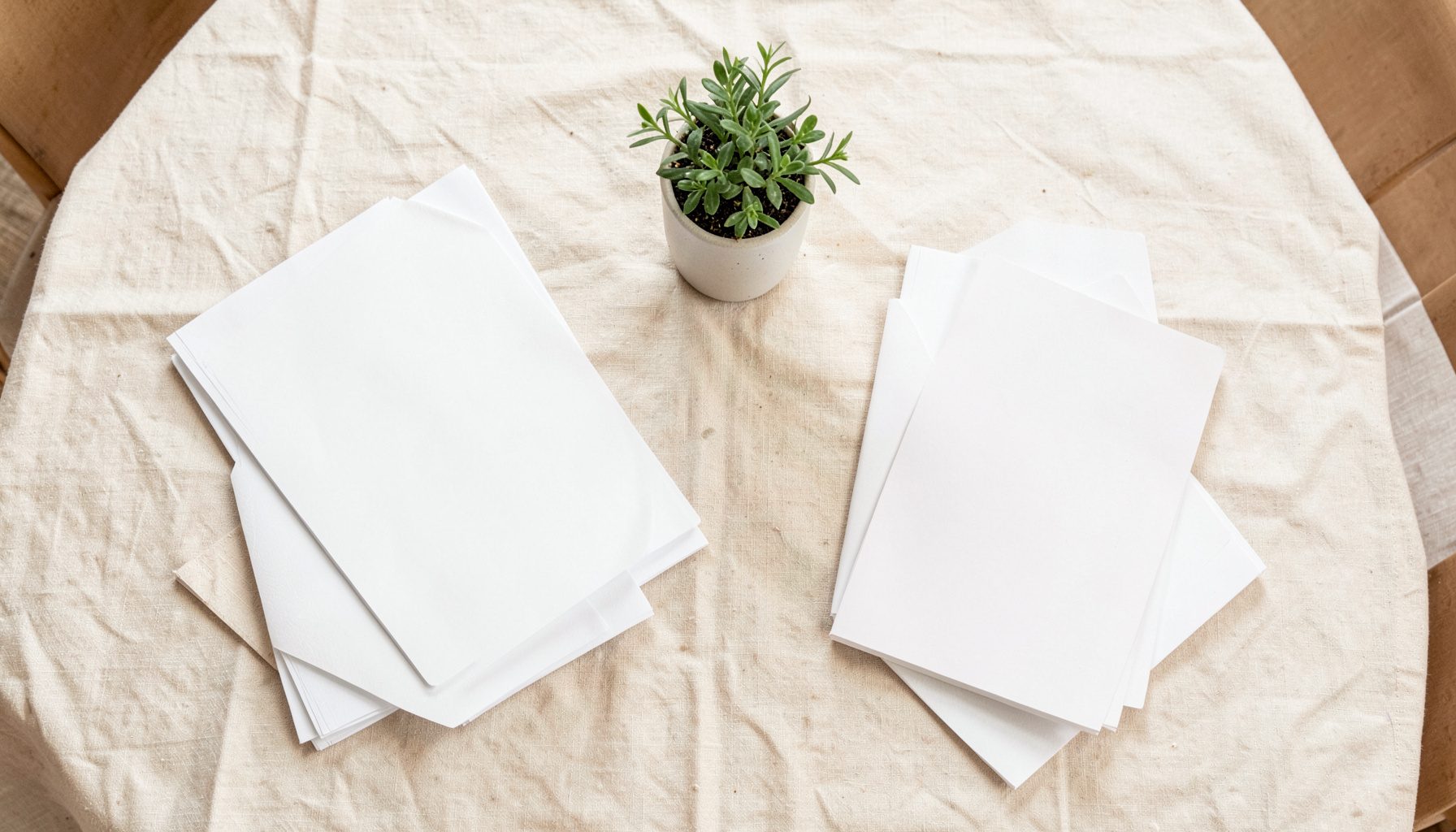 Top-down photograph of a neatly laid meeting table with paper notebooks, a ceramic mug, and a small potted plant on warm cream linen